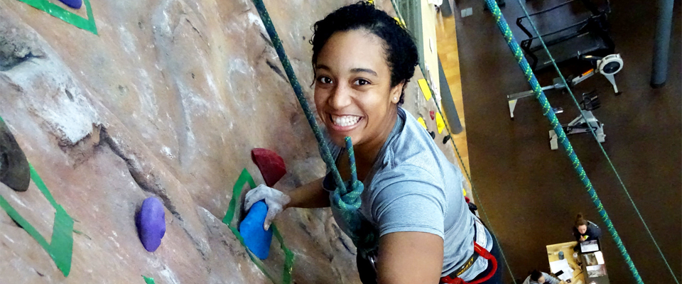 A climber at the Cary Street Gym climbing wall looks up at the camera with a smile