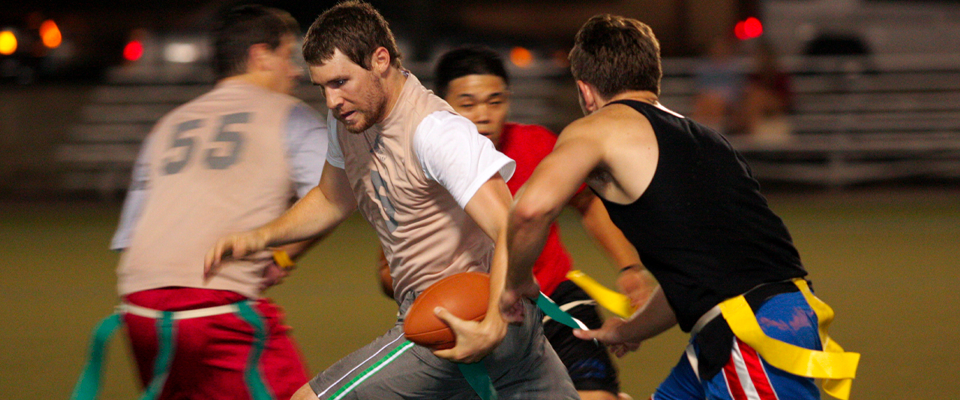 A flag football player holds the ball white two other players try to tear one of their flags