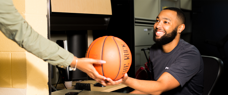 A RecWell facility attendant hands a basketball to a patron